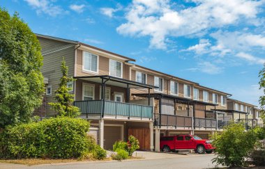 Güneşli bir günde güzel bir mahalle. Kasaba evleri için park yerindeki garaj kapılarında sıra var. Beton garaj yolu, garaj kapısı ve penceresi olan evin dışı. Garaj kapısı, kısa yol.
