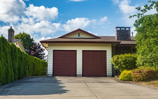 Double garage with short driveway in a sunny summer day. A perfect neighbourhood. Family house with wide garage door and concrete driveway in front. A beautiful large modern custom residential house