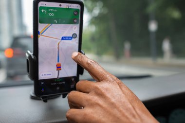 Arabada bir erkek ve akıllı telefon var. Adam, varış noktasına giderken telefonunda GPS navigasyon sistemi kullanarak araba kullanıyor. Nakliye, teknoloji. Harita navigasyonlu cep telefonu montajda sabitlendi.