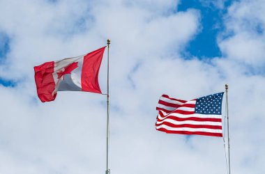 Kanada ve ABD bayrağı beyaz bulutlu mavi gökyüzünün arka planına karşı. Amerika ve Kanada ulusal bayrak kumaşı gökyüzünde dalgalanıyor. Amerikan ve Kanada bayrakları birlikte. Üst görünüm.