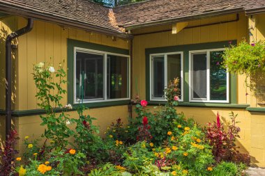 Güneşli bir günde güzel manzaralı bir ev. Renkli çiçekler ve pencereli bir ev. Geleneksel bir kır evinin önünde çok renkli çiçek açan güzel doğal bahçe.