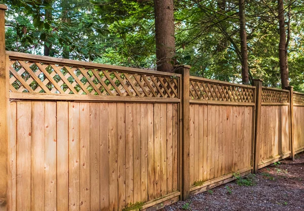 Nice new wooden fence around house. Wooden fence with green lawn in a sunny summer day. Street photo, nobody. Beautiful wooden fence around the house. Solid cedar fence