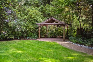 Bahçede yeşillik ve çimlerle çevrili Pavilion ya da pergola. Yaz parkında dinlenmek için ahşap bir çardak. Yeşil Ağaçlı Yürüyüş Yolu. Ağaçlı ve yeşil çimenli bir yaz parkında yol