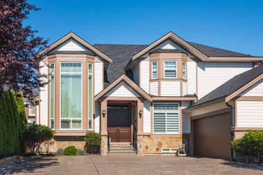 Güneşli bir günde gayrimenkul paravanı. Bahçesi güzel döşenmiş lüks bir ev ve banliyödeki garajdan garaja giden bir yol. Modern tasarım ev, yeni inşaat evi dış görünüş