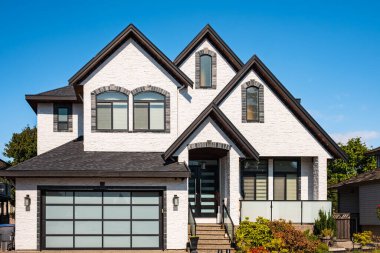 Güneşli bir günde gayrimenkul paravanı. Bahçesi güzel döşenmiş lüks bir ev ve banliyödeki garajdan garaja giden bir yol. Modern tasarım ev, yeni inşaat evi dış görünüş