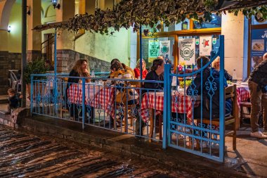 Kafe masaları ve yemek yiyen turistlerle dolu eski bir cadde. Arnavutluk 'un Cirokaster kentindeki sokak restoranları. Arnavutluk 'un eski kenti 27 Ekim 2023' te gece çalışan açık hava restoranları