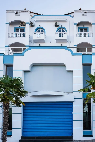 Traditional Greek style architecture. White blue houses with palm trees. Mediterranean residential building. Exterior of a white mediterranean-style house with a blue door and a window, and palm trees