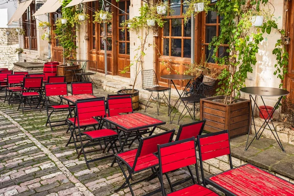 Outdoor restaurant terrace with colorful wooden tables and chairs. Old fashioned restaurant patio furniture. Traditional outdoors cafe on cobblestone street. Cozy old street in Gjirokaster Albania