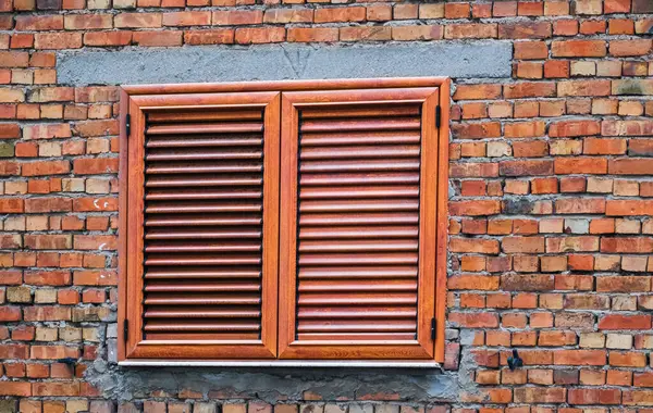 Window and shutters on a red brick house wall. Wooden window with shutters isolated exterior. brown wooden exterior shutters. Outdoor shutters.