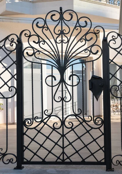 Forged decorative gates. Iron door, gate with wrought ornament on it. Black metal garden entrance gates. Street photo, nobody
