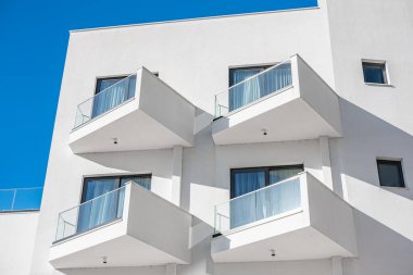 Mavi gökyüzü arka planlı modern beyaz apartman. Binanın güzel modern mimarisi. Soyut Mimarlık. Mimari detay balkonlu ve pencereli modern cephe binası