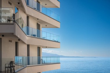 Mavi gökyüzü ve deniz altyapısı olan modern beyaz bir apartman. Binanın güzel modern mimarisi. Mimari detay balkonlu ve pencereli modern cephe binası