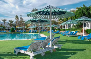 Tropik tatil köylerinde palmiyeli güzel bir yüzme havuzu. Yüzme havuzu bulutlu mavi gökyüzü. Afrika Mısır. Rahatlayın ve huzurlu titreşimler, şezlonglar şemsiye ve palmiye ağaçları altında. Lüks seyahat tatili