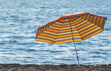 Plajda havlunun yanında çizgili plaj şemsiyesi. Güneşli bir günde plaj şemsiyesi. Güneş koruma şemsiyesi. Hiç kimse, metin için boşluk kopyala, seyahat fotoğrafı