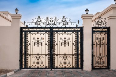 Büyük, çift katlı metal bir kapı. Çift işlemeli demir kapı. Demir kapı ve taş sütun satmış. Kırsal araziye siyah dövmeli demir giriş kapıları. Hiç kimse, sokak fotoğrafı.