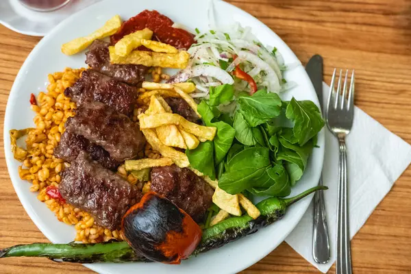 Turkish meatballs, Turkish Food Kofte or Kofta with red peppers,tomato, french fries and onion. Delicious Turkish Traditional Kebab Kofte with pilaf on white plate, meatballs. Spicy meatballs Kebab