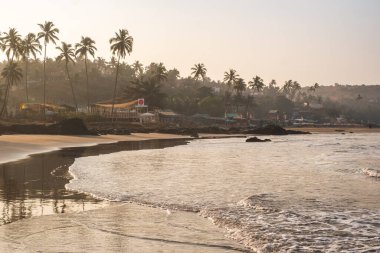 Vagator ya da Ozran sahilinin kuzey Goa, Hindistan 'daki panoramik manzarası. Sabahın erken saatlerinde sahildeki palmiye ağaçlarının ve restoranların güneş doğuşundan önce.