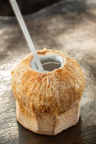 Coconut drink with straw on a wooden table. Tropical fresh coconut water with straw. Refreshing coconut cocktail. Nobody, selective focus
