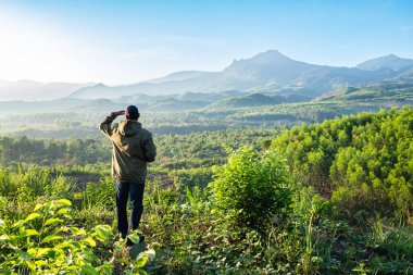 Bir yürüyüşçü, dağlık bir yabanda, Da Lat Vietnam 'da gün doğumunda bir sükunete bakıyor. Dağın tepesinde duran bir adam uzaklığa bakıyor. Bir vadi ve dağ sırasına bakan bir yürüyüşçü.