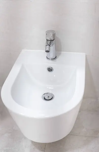 stock image Bidet in a bathroom. Generic bathroom with ceramic bidet washing basin. White bidet screwed to a beige tiled wall in the bathroom, close-up, nobody