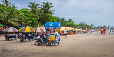 Kuzey Goa 'daki Arambol plajı manzarası. Palmiye ağaçlı Arambol plajı, Hint ve yabancı turistli plaj şemsiyeleri. Nort Goa 'nın popüler turistik merkezi. Seyahat fotoğrafı, uzayı kopyala. 7 Eylül 2024
