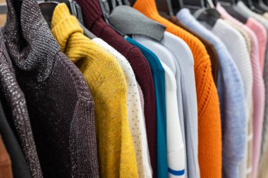 Kadın giysileri - sonbahar kış koleksiyonu. Moda örgü giysiler, askılarda asılı sergilenmek için. Sıradan kadın kazakları, indirim sezonu. Çok renkli, kalın kazaklar. Tırabzanda kadın giysileri.