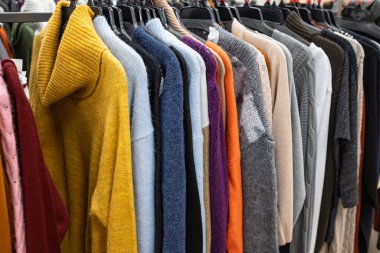 Kadın giysileri - sonbahar kış koleksiyonu. Moda örgü giysiler, askılarda asılı sergilenmek için. Sıradan kadın kazakları, indirim sezonu. Çok renkli, kalın kazaklar. Tırabzanda kadın giysileri.