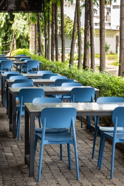 Outdoor cafe with wooden tables, stools on a city street. Wooden tables and blue chairs set up at an outdoor cafe on a sunny summer day. A cozy outdoor dining area. Nobody, street photo clipart