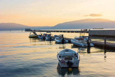 Arnavutluk 'un Vlore kenti yakınlarındaki limanda gün batımında, sürat tekneleri turizm için kullanılıyor. Su cephesi Tekne gezisi. Vlore Dağlar ve İyon Denizi ile çevrilidir. 11 Kasım 2024