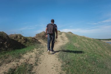Güneşli bir günde sırt çantasıyla tepeye tırmanan bir adam. Tatilde olan bir adam dışarıda faaliyet gösteriyor. Dağda yürüyüş. Açık hava aktivitesi, Vlore. Seyahat konsepti, uzayı kopyalamak. 7 Kasım 2024