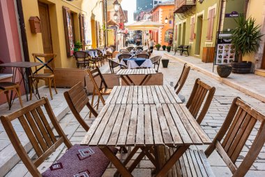 Ahşap masalı açık bir kafe, şehir caddesinde tabure. Arnavutluk 'un Vlore kentinin tarihi merkezi. Renkli binalar, dükkanlar ve restoranlarla eski kasabadan güzel bir yürüyüş. Seyahat fotoğrafı.