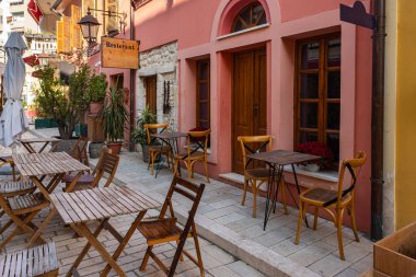 Ahşap masalı açık bir kafe, şehir caddesinde tabure. Arnavutluk 'un Vlore kentinin tarihi merkezi. Renkli binalar, dükkanlar ve restoranlarla eski kasabadan güzel bir yürüyüş. Seyahat fotoğrafı.