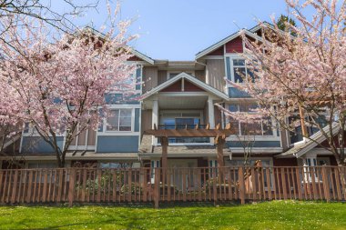 Baharda çiçek ağaçlarıyla güneşli bir günde Harici Emlak Cephesi. Bahçe ve çitlerle döşenmiş büyük lüks bir ev. Modern tasarım ev.