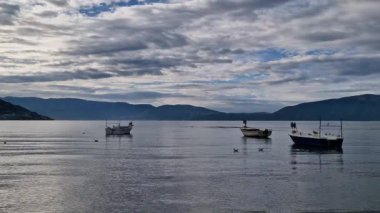 Gölün kıyısında ahşap balıkçı tekneleri. Denizde yüzen balıkçı tekneleri ve arka planda dağları Vlore Arnavutluk. Denizde huzurlu bir sabah. Seyahat videosu