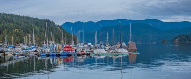 Arka planda yatlar ve dağlar olan güzel bir manzara. Marinada park etmiş yelkenli ve yatlar. Çok güzel. Lüks yaşam tarzı, macera, yelken, Kanada İngiliz Kolumbiyası. 22 Kasım 2022