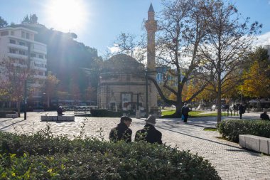 Exterior view to Muradie mosque in Vlore Center, Albania. People relaxing in the park. Muradie Mosque is a 16th century historical landmark. Travel photo. December 3, 2024 clipart