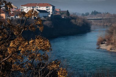 Sonbahar günü Moraca nehir kıyısındaki Podgorica kenti. Balkanlar ve nehir manzarası. Moraca Nehri ile çevrili Podgorica manzarası, yeşillik, konut binaları ve tepelerle çevrili. Karadağ