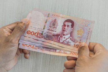 Tayland baht 'ını elinde tutan adam. Tayland bahtı nakit para veriyor. Tayland Bankası Not 1000 Baht kağıt nakit ışık arka planda. Yakından 1000 Tay baht banknot tutuyor.
