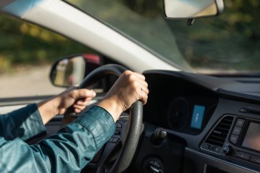 İki elini de direksiyona koyan kişi. Kadın sürücü elleri direksiyonda. Şehirde araba süren bir kadın. Yollarda ilerleyen modern aracın iç görünümü.