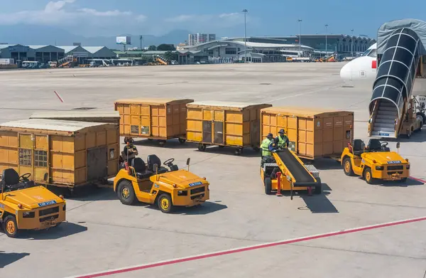 Bagajlar için yük arabası yükleyicisi. Cam Ranh Uluslararası Havalimanı Vietnam 'da bagajlı sarı araba. Yolcu uçağının yanındaki sarı kamyonlar, uçuş öncesi havaalanı - 27 Mart 2024