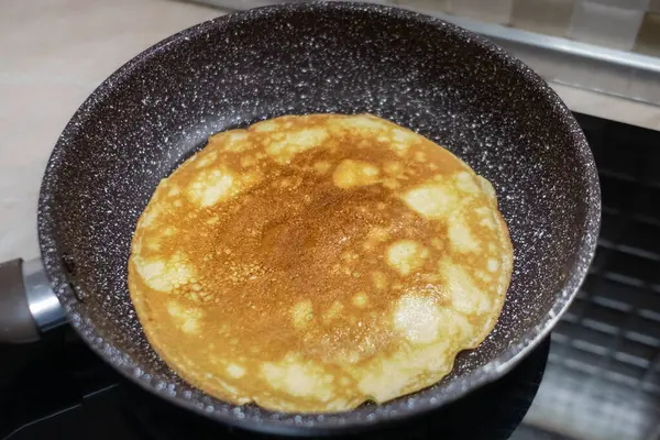 Krep yapıyorum. Kızartma tavasında krep hamuru. Ev yemeği. İndüksiyon sobada tavada nefis ince bir krep, yakın plan. Büyük Altın Krep Yapışmayan Siyah Tavada Pişiyor