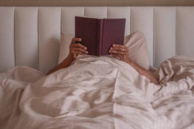 Adam yatakta kitap okuyor. Evdeki yatakta kitap okuyan genç bir adam. İnsanlar Akşam Rahatlaması, Hobiler, Boş Zaman, Uyku ve Dinlenme Konsepti