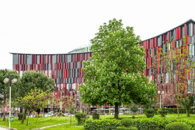 Birçok penceresi olan ticari bir bina. Arnavutluk 'un Tiran kentinde önünde yeşil ağaçlar bulunan renkli ve çağdaş bir binanın cephesi. Soyut çok renkli modern mimari. Seyahat fotoğrafı, editör - 8 Nisan 2025