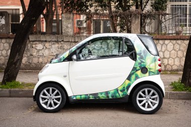 Smart Car Tiran Arnavutluk 'ta caddeye park etmiş. Yol kenarındaki yeşil ağaçların altında küçük şık bir araba sakin bir banliyö sokak editörü, 8 Nisan 2025