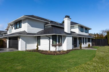 Güneşli bir günde gayrimenkul paravanı. Banliyöde manzarası güzel olan büyük lüks bir ev. Lüks, büyük, güzel bir ev. Önünde yeşil çimenler olan geniş bir aile evi.