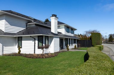 Güneşli bir günde gayrimenkul paravanı. Banliyöde manzarası güzel olan büyük lüks bir ev. Lüks, büyük, güzel bir ev. Önünde yeşil çimenler olan geniş bir aile evi.