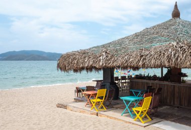 Beyaz kumlu sahildeki rahat kafe, yaz tatili konsepti. Plajda, güneşli yaz gününde tahta sandalyeli ve masalı bir restoran. Tropik plaj manzarası. Yaz tatili konsepti. Seyahat fotoğrafı.