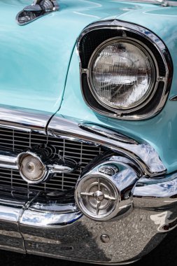 Antika bir aracın ön far yakın görüntüsü. Üzerinde kaput süsü olan eski bir turkuaz arabanın far ve ızgarası. Sokak fotoğrafı, kimse yok.