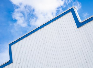 Geometrik soyut yapı mimarisinin düşük açılı görüntüsü. Binanın çatısı ve gökyüzü. Mavi gökyüzüne ve beyaz bulutlara karşı ahşap binanın tepesinde. Modern mimari. Asgari tasarım