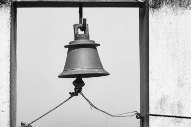 Pirinç zili açık havada. Çan kulesinin mimari detayları siyah beyaz. Eski şehrin limanındaki beton bir yapıdan sarkan eski metal çan..